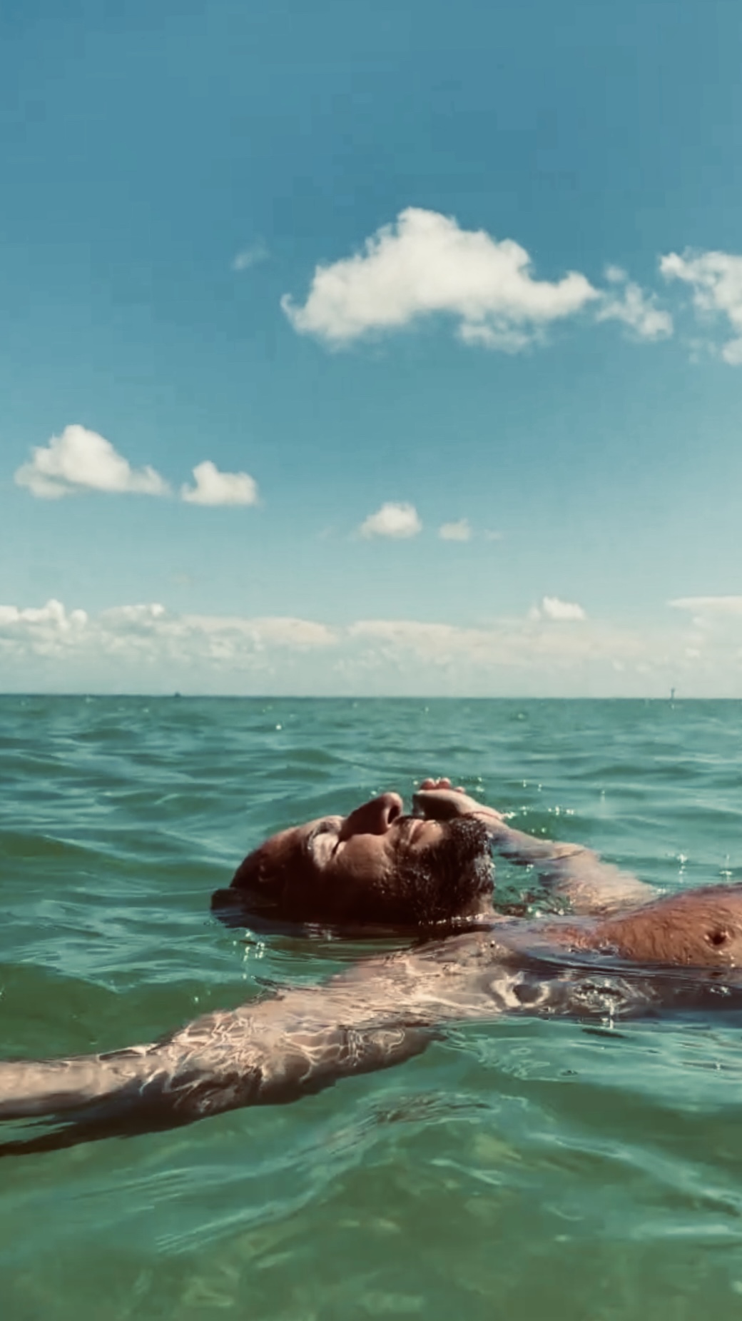 Troy Jason Valls floating on his back in calm turquoise water under a bright sky