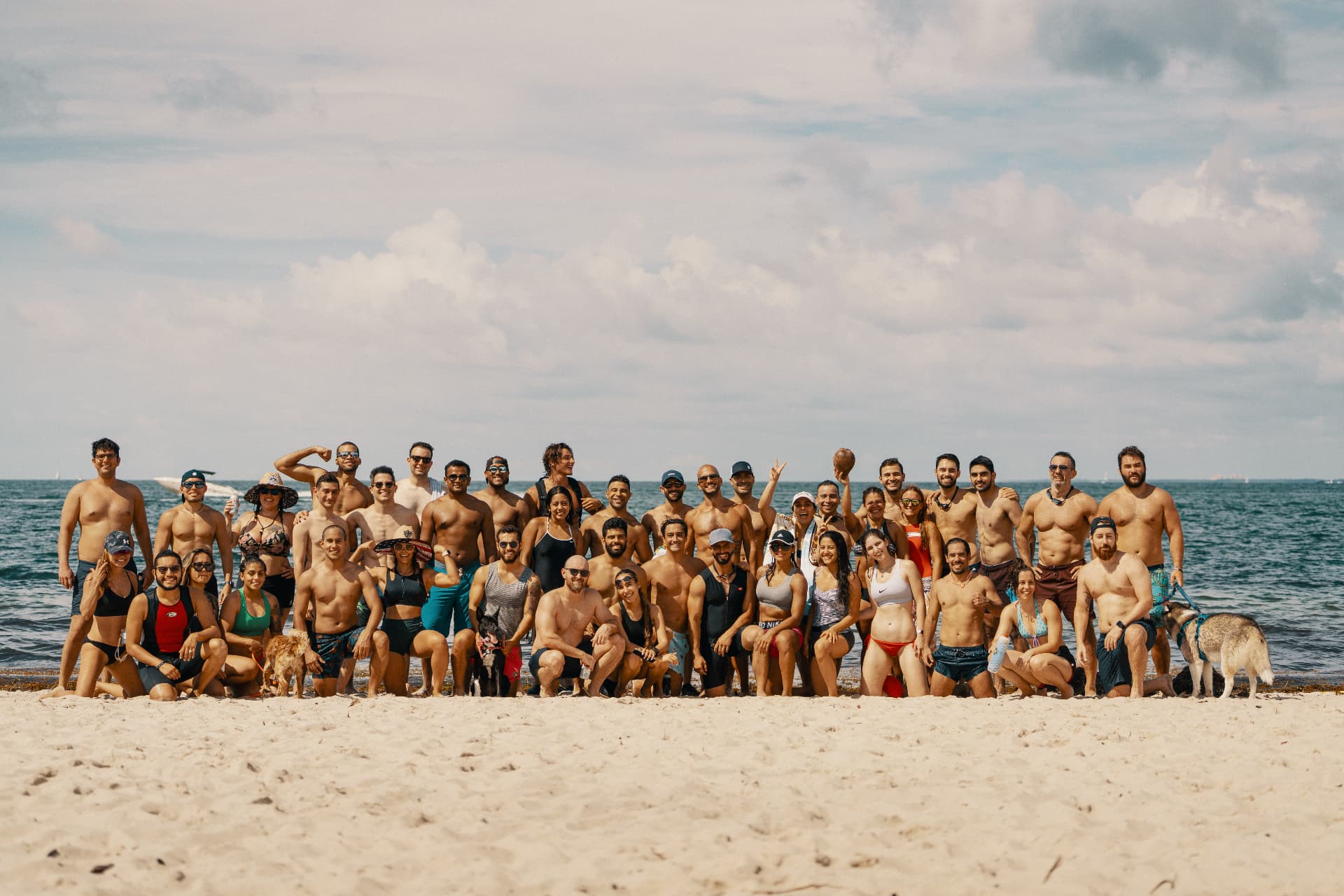 A large group from the Move. Lift. Live. community standing together on the beach at the water's edge