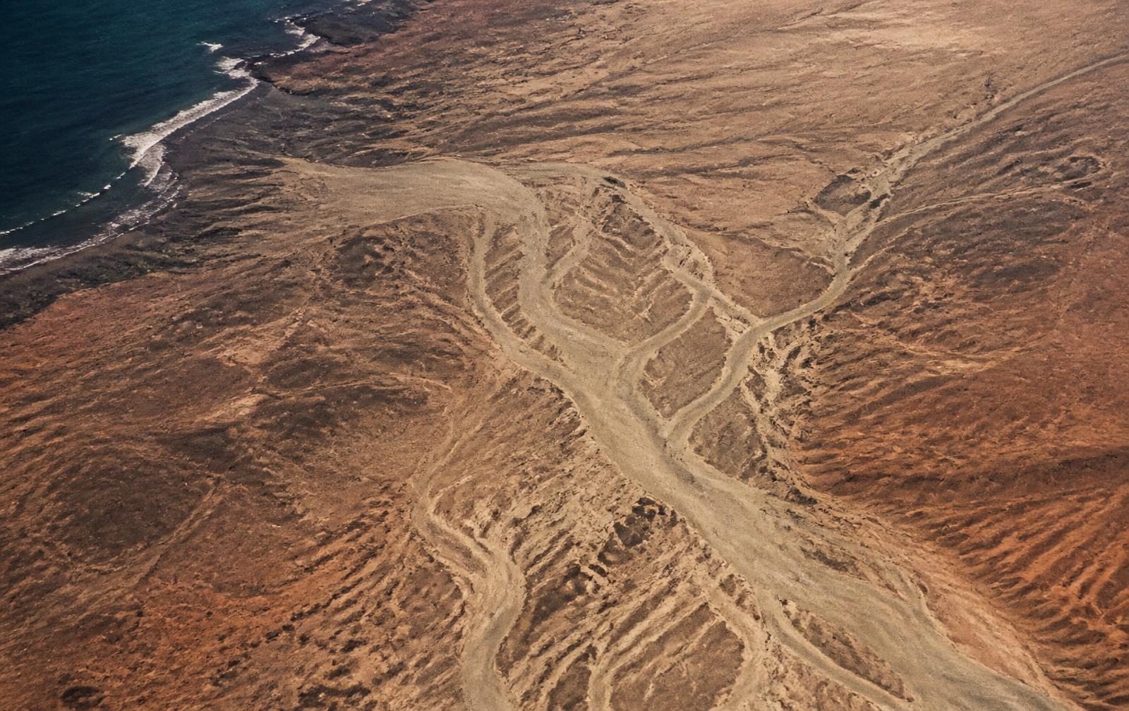 Aerial view of dry branching channels cut into warm clay-coloured coastal earth